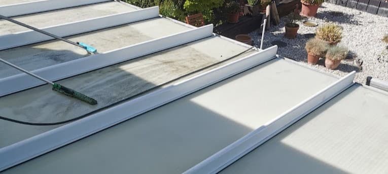 Ein Dach wird mit einer Teleskopstange und einer Buerste gereinigt. Die Dachplatten sind teilweise sauber, teilweise noch verschmutzt.