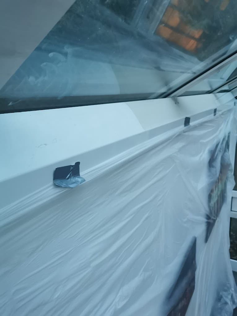 Ein Fenster ist mit einer Plastikfolie abgedeckt, die mit Klebeband befestigt ist, um es vor Malerarbeiten zu schützen. Die Folie ist zerknittert und teilweise transparent.