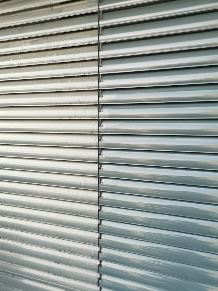 Ein Vorher-Nachher-Vergleich von Jalousien, wobei die linke Seite schmutzig und die rechte Seite sauber ist. Die Jalousien sind horizontal angeordnet und aus Metall.